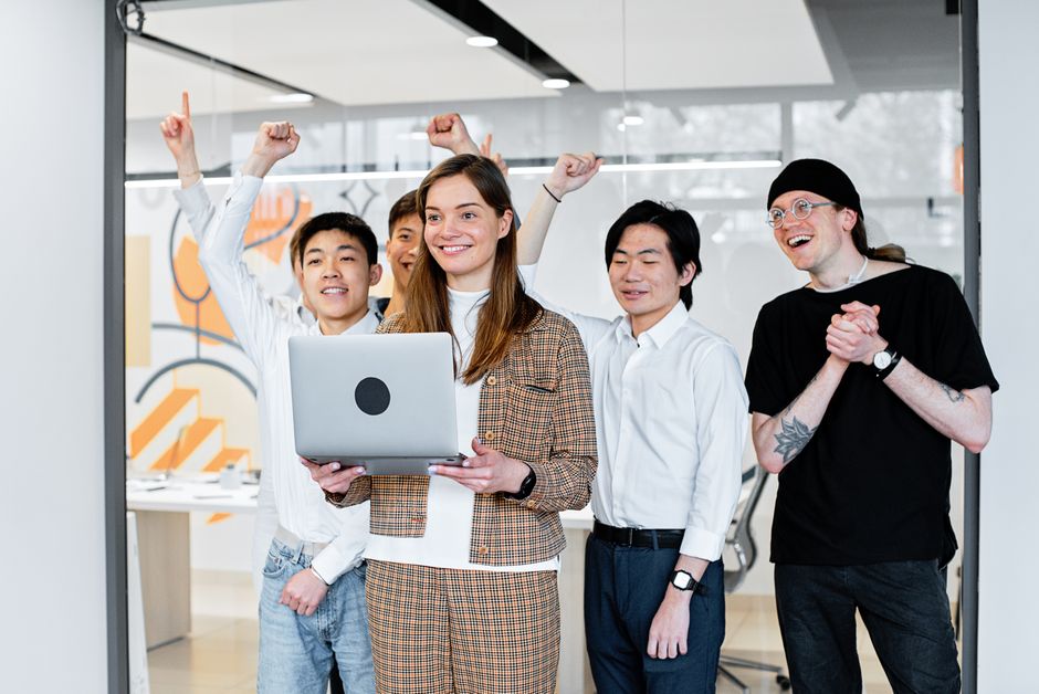 Group of diverse colleagues celebrating success while collaborating on a laptop indoors.