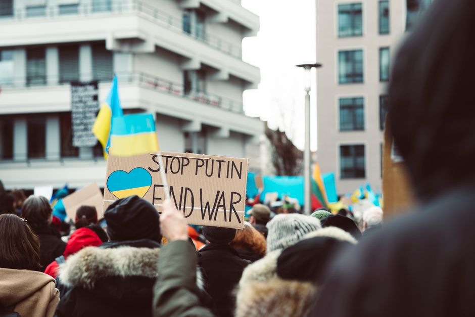 Peaceful protest in an urban setting featuring anti-war signage and Ukrainian flags.
