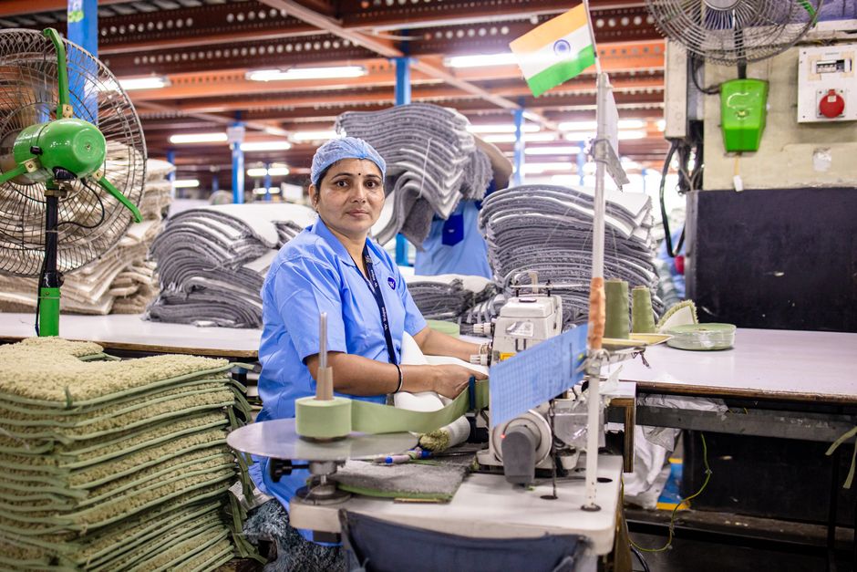 A female factory worker sewing textiles in an Indian factory, surrounded by fabrics.