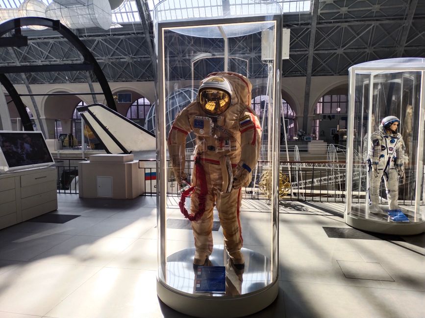 Combinaisons spatiales historiques exposées dans une galerie musée bien éclairée.