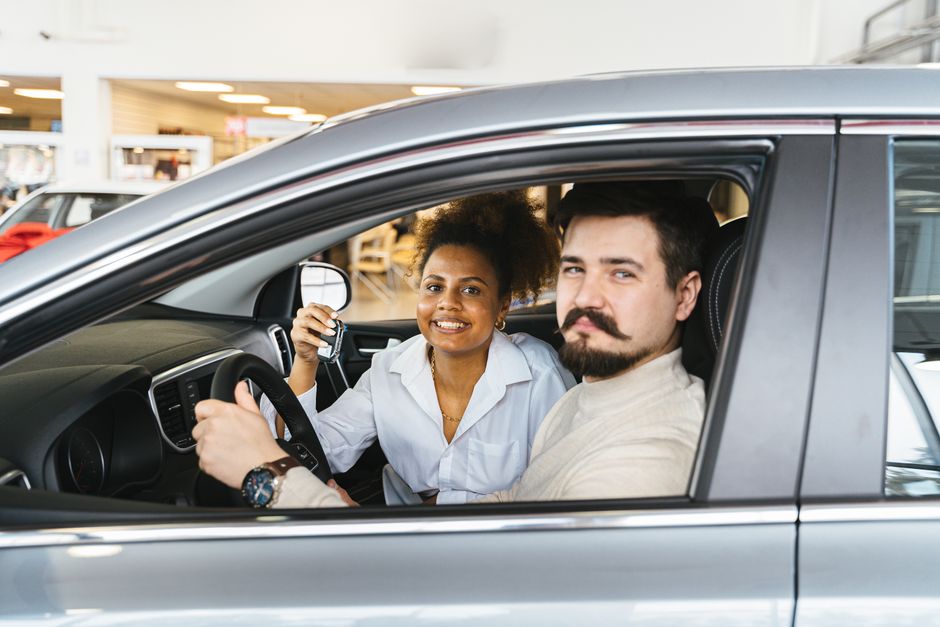 Un couple souriant assis dans une voiture neuve avec les clés