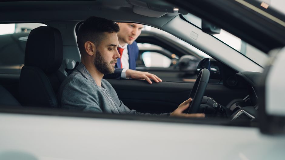 Un homme examine l'intérieur d'une voiture avec un vendeur.