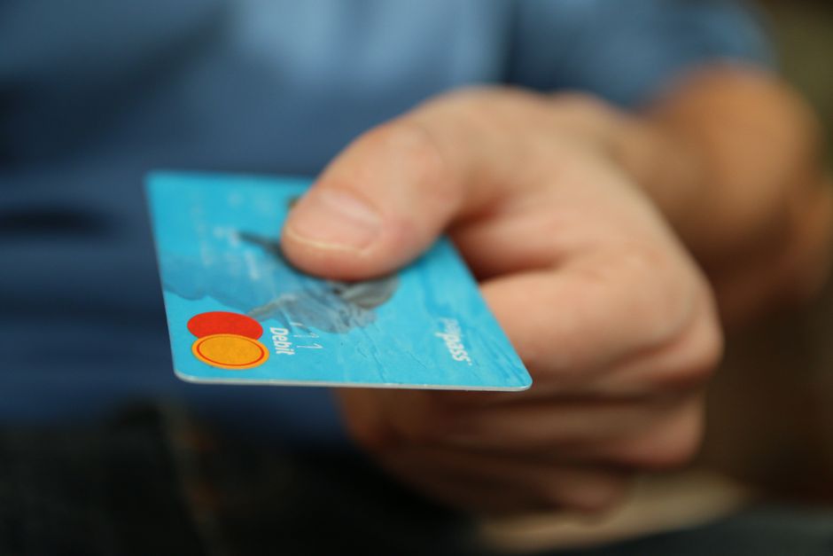 Une main tend une carte bancaire bleue pour effectuer un paiement.