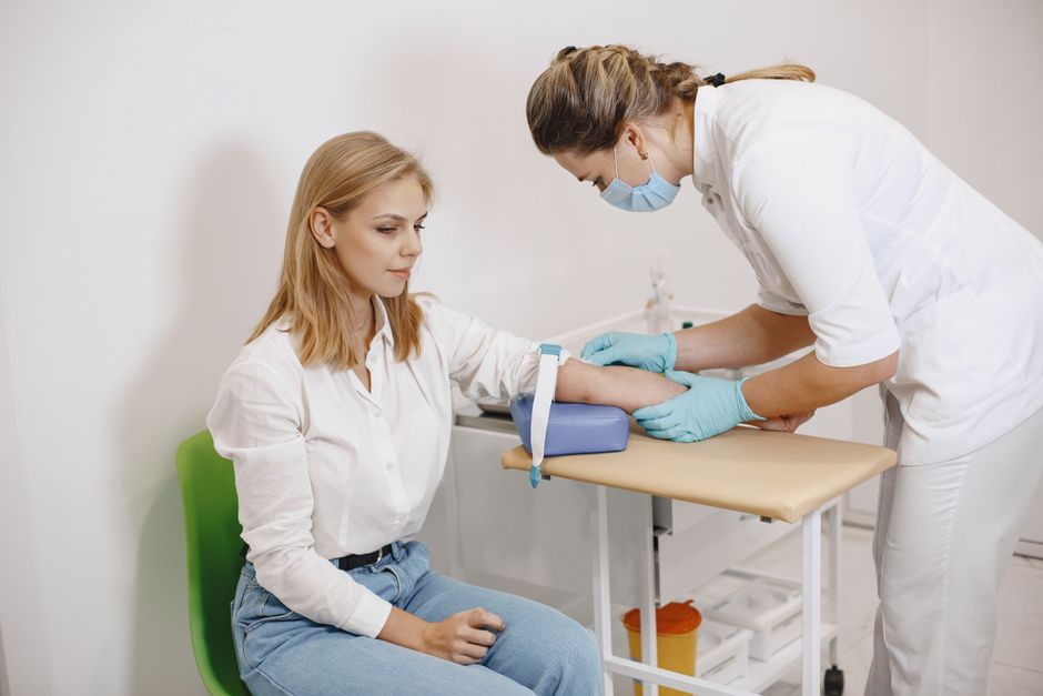 Une infirmière effectue une prise de sang sur une patiente assise en consultation médicale.