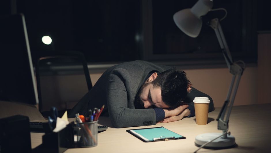 Un homme en costume dort sur son bureau près d'une tasse de café.