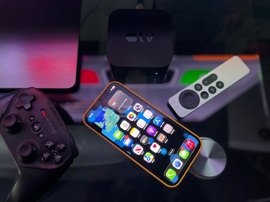 iPhone posé près d'une Apple TV et une manette de jeu sur surface sombre