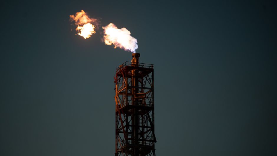 Une cheminée industrielle crache une flamme orange dans la nuit