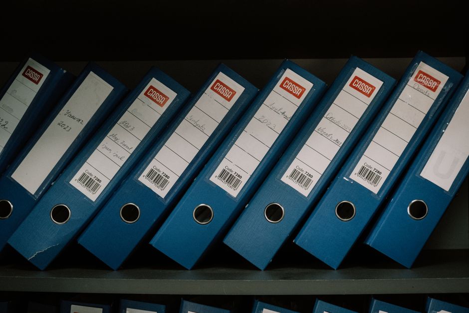 Des classeurs de bureau bleus rangés avec étiquettes de dates et noms.