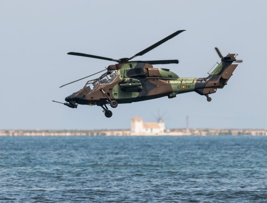Un hélicoptère militaire en vol au-dessus de l'eau près d'une côte.