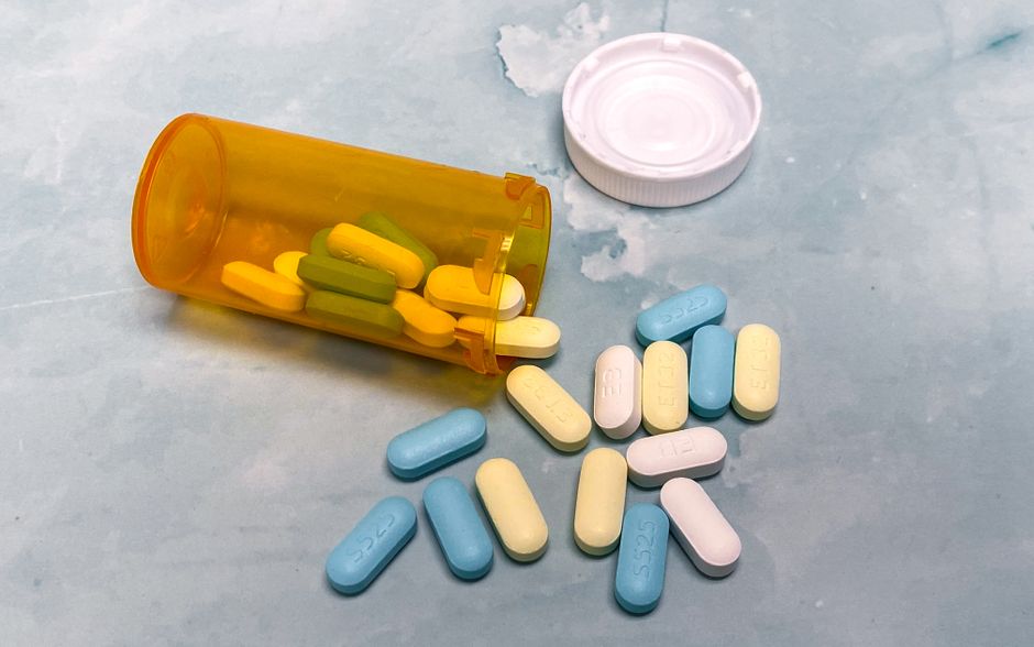 Un flacon de médicaments ouvert avec des comprimés colorés sur fond bleu clair.