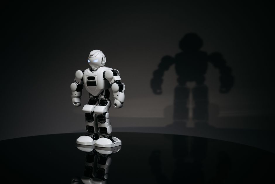 Un robot humanoïde blanc et noir en studio, projetant son ombre