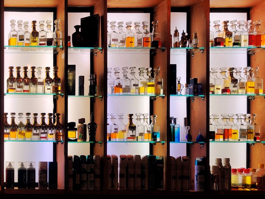 Différents flacons de produits parfumés disposés sur des étagères en bois et verre.