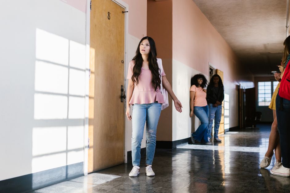 Adolescente dans un couloir d'école, l'air pensif, entourée de camarades