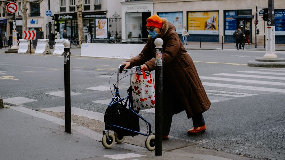 Une femme âgée avec masque traverse une rue de ville