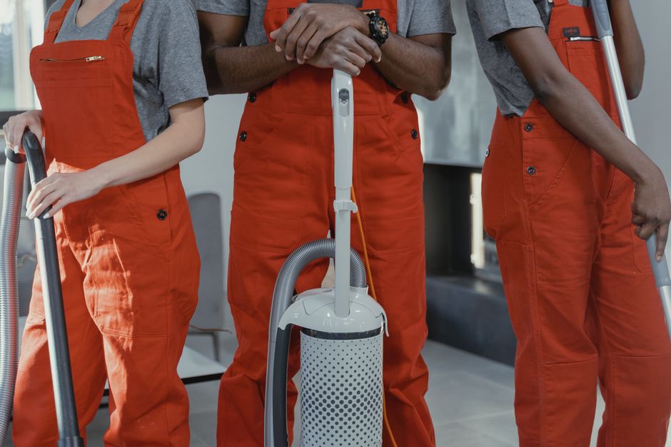 Trois techniciens en combinaison rouge inspectent une pièce avec des outils.