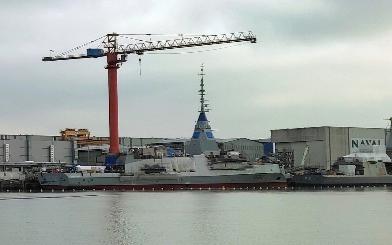 Une frégate en construction le long d'un quai, grue de chantier au-dessus