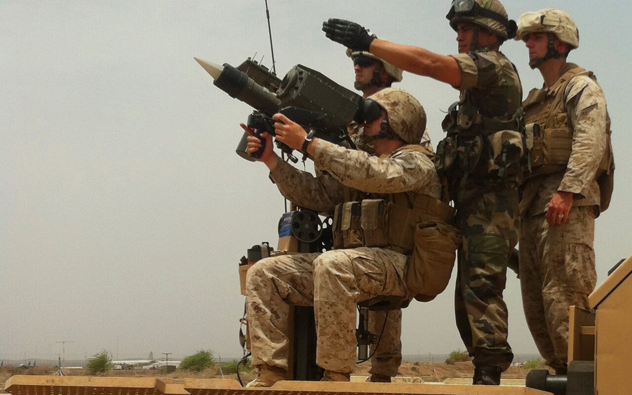 Des militaires en tenue désert pointent un lanceur de missiles sol-air monté sur affût, un servant à l'oculaire