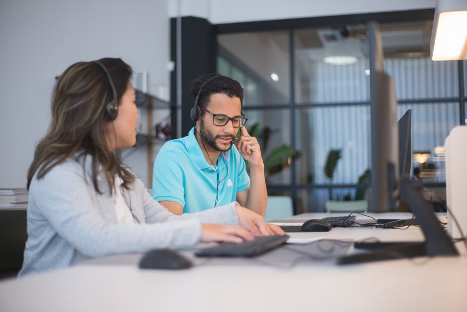 Deux employés de centre d'appels travaillent ensemble à leurs postes informatiques avec casques.