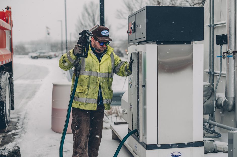 Un homme fait le plein d'essence à une pompe de station-service en hiver.
