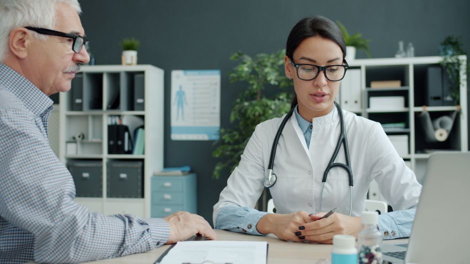 Un professionnel de santé discute avec un patient senior dans un bureau.