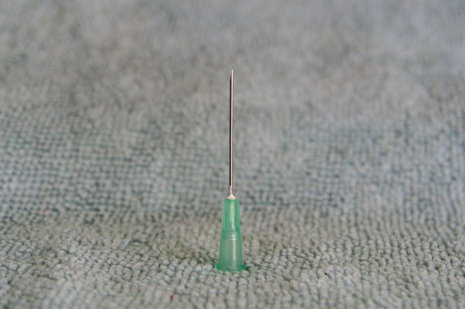 Aiguille médicale fine avec embout vert sur surface textile