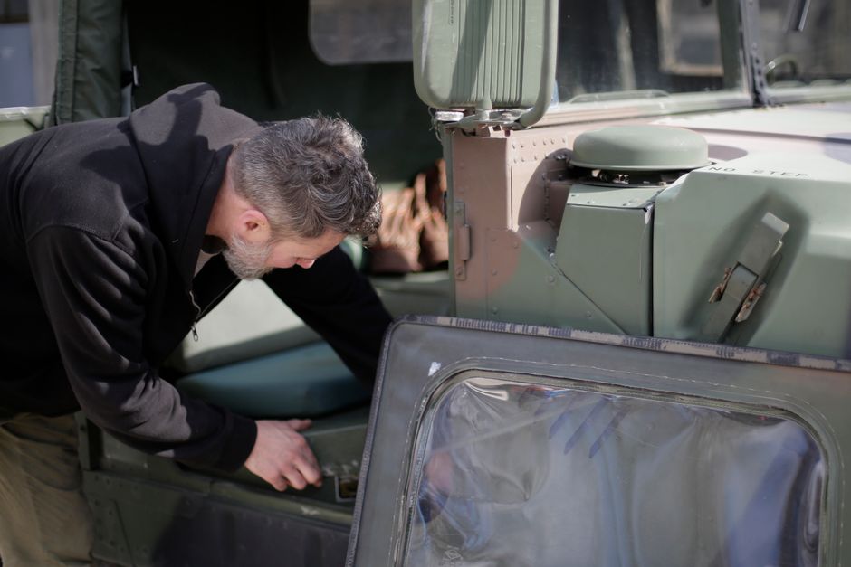 Un mécanicien en tenue de travail contrôle les détails d'un véhicule militaire.