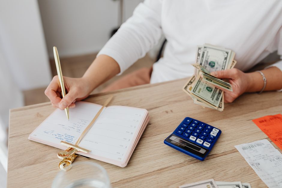 Personne tenant des billets et notant des calculs sur un agenda avec une calculatrice