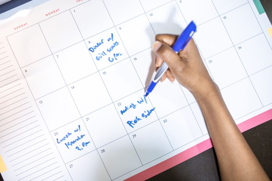 Personne notant des rendez-vous sur un calendrier avec un stylo bleu