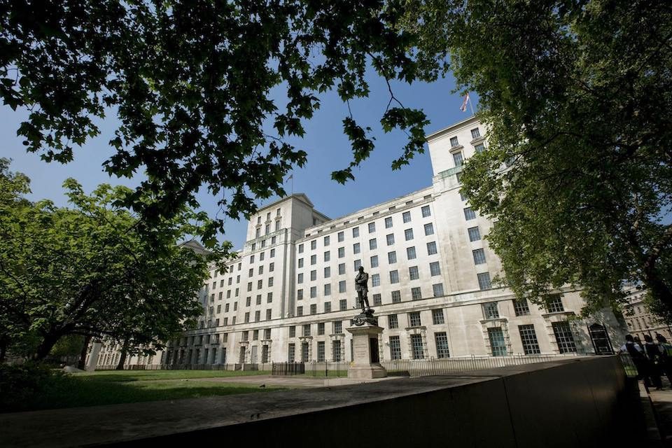 Bâtiment administratif de pierre claire à plusieurs étages entouré d'arbres sous ciel bleu