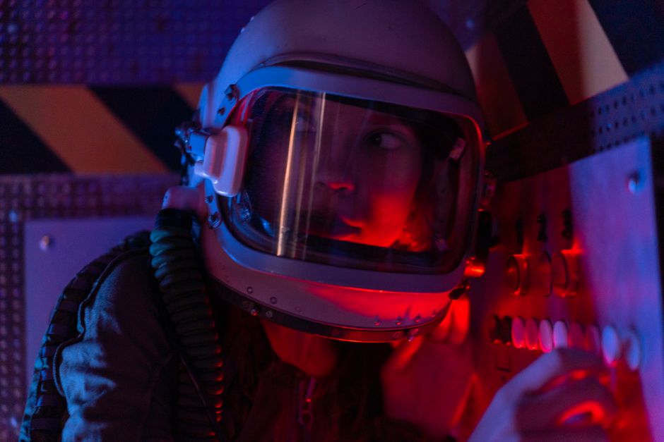Une astronaute en combinaison spatiale dans une salle de contrôle éclairée de rouge.