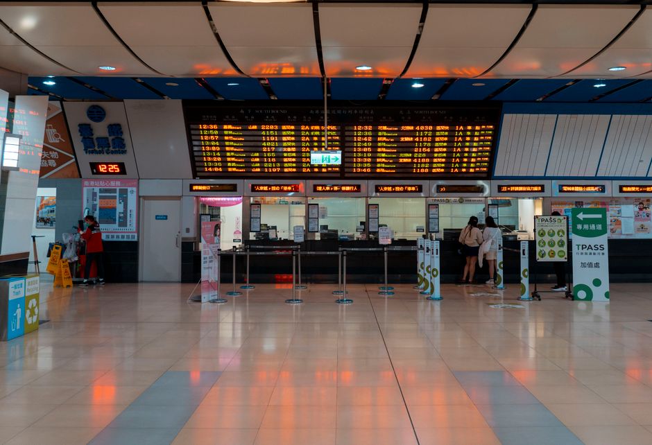 Intérieur d'une gare avec panneau horaire numérique et guichets de tickets.