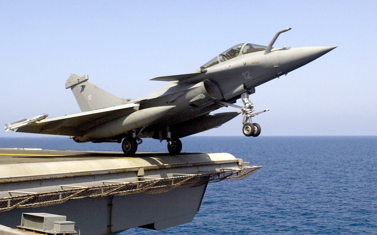 Un avion de combat quitte la piste oblique d'un porte-avions, train sorti au-dessus de la mer