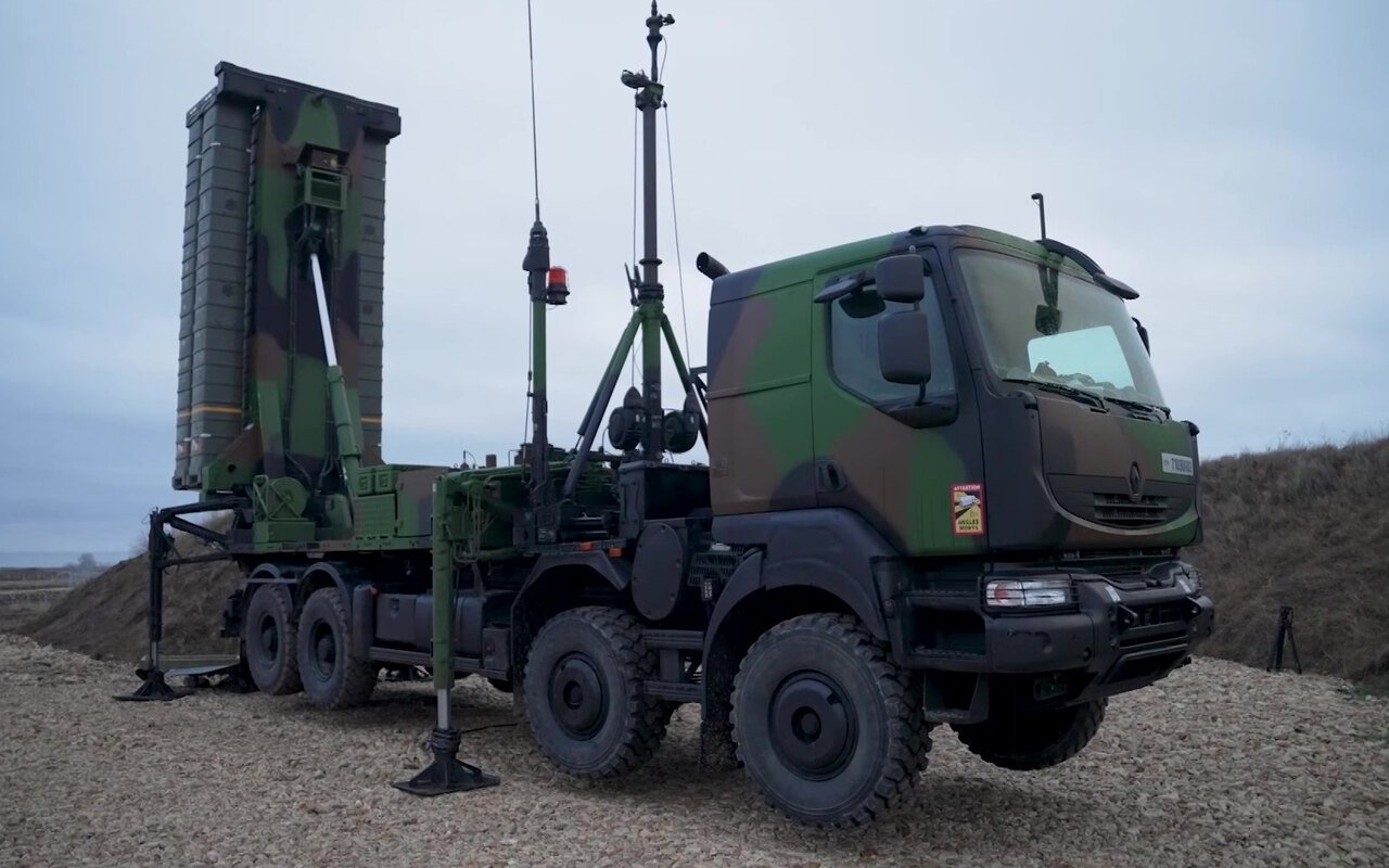 Un lanceur de missiles sol-air aux conteneurs dressés vers le ciel, stabilisé sur un terre-plein de gravier