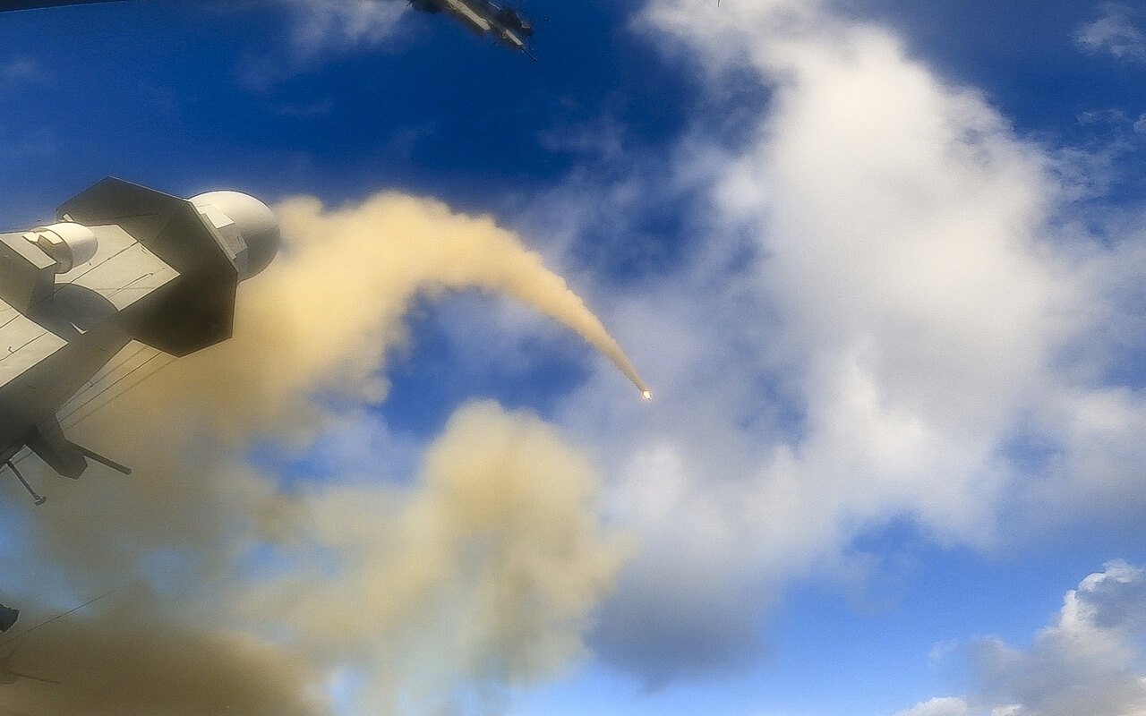 Un missile laisse une traînée de fumée au-dessus de la mâture d'une frégate, pointe incandescente visible